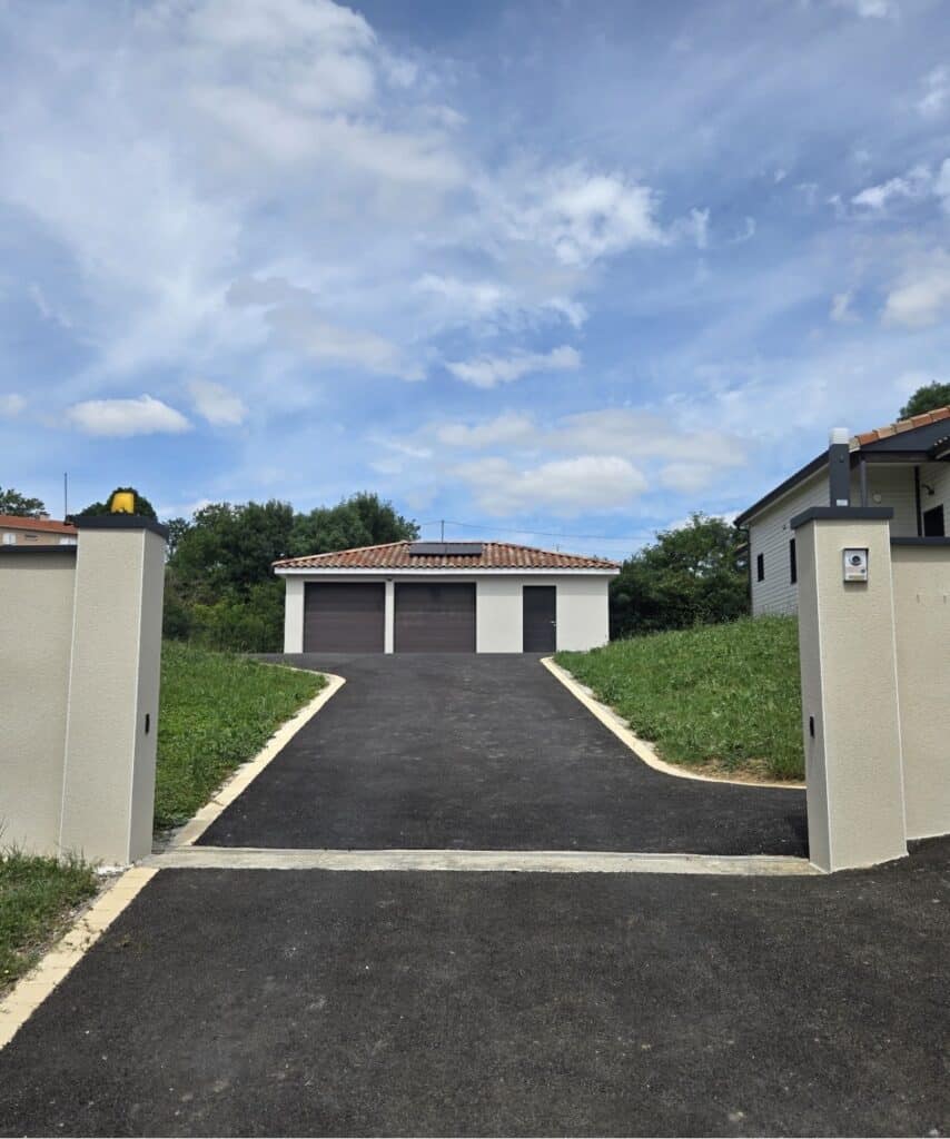 Aménagement d'une Allée en Asphalte avec Garage Moderne Allée en asphalte noir menant à un garage blanc avec deux portes brunes sous un ciel bleu nuageux.